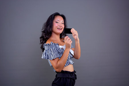 Pretty Asian girl with cute face showing a black card in her hand, isolatedの写真素材
