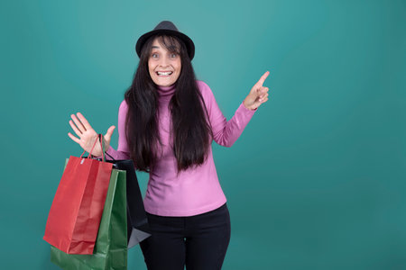 Smiling woman holding paper shopping bags, wearing pink sweater and black hat, isolated.の写真素材