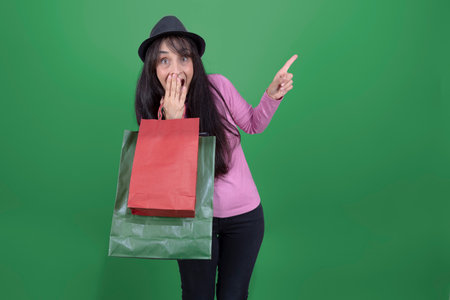Smiling woman holding paper shopping bags, wearing pink sweater and black hat, isolated.の写真素材