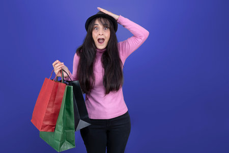 Smiling woman holding paper shopping bags, wearing pink sweater and black hat, isolated.の写真素材