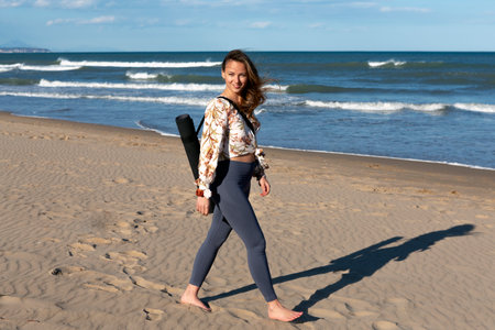 pretty woman walking barefoot on the beach with mat slung over her shoulderの写真素材