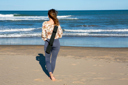 young woman seen from behind, standing on the beach looking out to seaの写真素材
