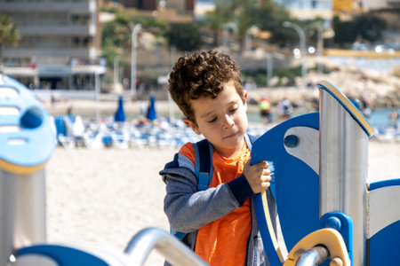 curly-haired boy playing in playground facilities located on the beachの写真素材