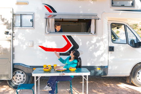 woman sitting at camping table next to motor home and child at windowの写真素材