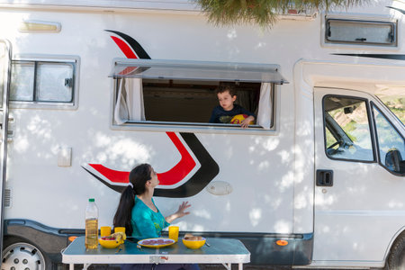 woman at camping table next to her motor-home and child in the windowの写真素材