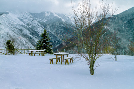 park without people in mountain viewpoint, in winter day with spectacular views to the bottom of snowy mountains, wooden benches and tables covered by thick layer of snowの写真素材