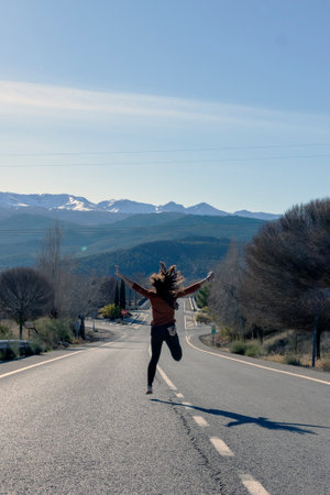 photo of woman seen from behind jumping in the middle of roadの写真素材
