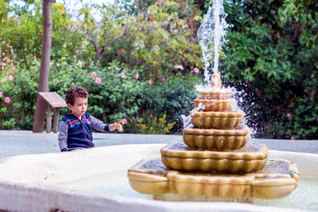 beautiful child playing with a leaf next to a fountainの写真素材