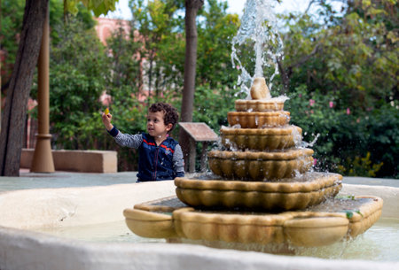 child playing with a leaf next to a fountainの写真素材
