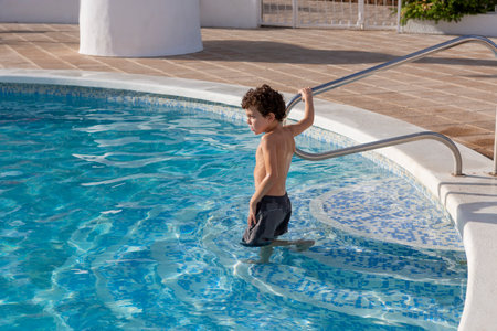 Young boy enjoying a swim in a residential pool, holding onto the ladder, surrounded by clear blue water.の写真素材