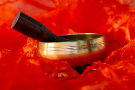 Close-up of a golden Tibetan singing bowl with wooden mallet, placed on vibrant orange fabric for spiritual and meditative use.の写真素材