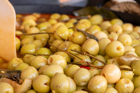 Close-up of pitted green olives marinated with herbs and spices, displayed in brine at a traditional Spanish market.の写真素材