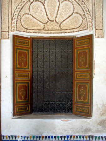 Traditional Moroccan window with painted wooden shutters and decorative wrought iron lattice, framed by intricate Arabic stucco patterns.の写真素材