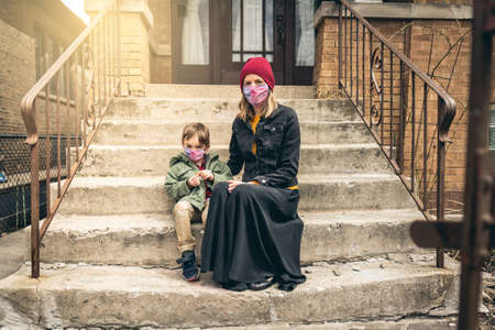 Mother and son sitting on the front steps with face masks on during quarantineの写真素材