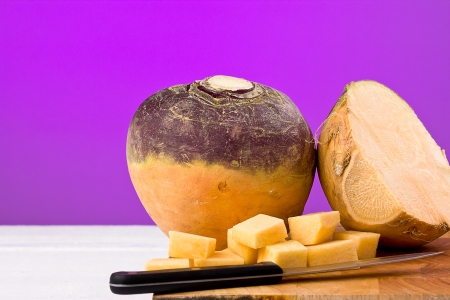 Large Swede chopped into square chunks on a chopping board with purple background and copy space.    の写真素材