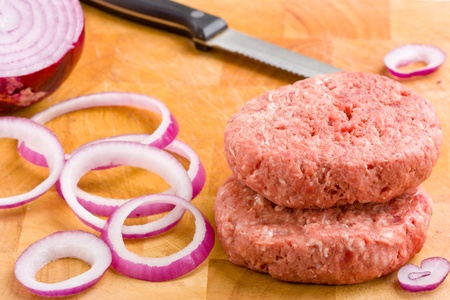 Two raw beef burgers with tasty red onion prepared on chopping board with knife. shallow depth of...