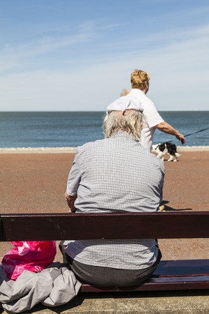 Llandudno, Wales, UK - May 17, 2014: Elderly man protects his balding head with a knotted handkerchief from the hot sunshine whilst sitting on wooden bench on Llandudnos north promenade in Wales U.Kのeditorial素材