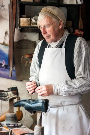 IRONBRIDGE, ENGLAND - JULY 21 2012 : Man dressed as Victorian cobbler  re-enacting his shoe mending duties at the Blists Hill Museum set in recreated streets and is a popular tourist attraction. Ironbriidge, Shropshire, England.のeditorial素材