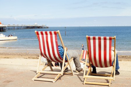 People sitting in deckchairs at Llandudno seaside holiday resort looking out to sea. Image taken from behindのeditorial素材