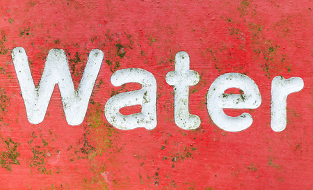 Red signage with the word water painted in white letters. An old metal sign covered in green algae scratches and rustの写真素材