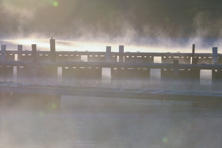 Boat Pier at Sunrise with Mist Lifting from Calm Lake Waterの写真素材