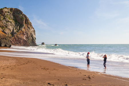 Two females getting their feet wet at the beach on a sunny day in Marin County Beachのeditorial素材