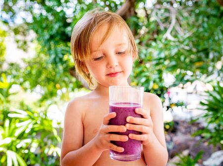 Healthy boy drinks delicious fruit smoothie outside during summer.の写真素材