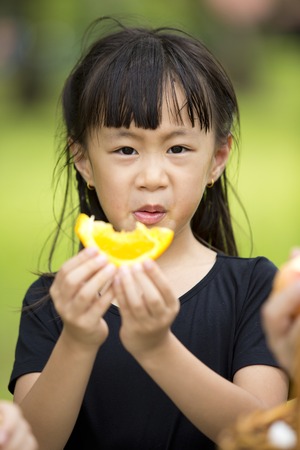 Asian young girl eating orange in parkの写真素材