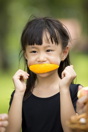 Asian young girl eating orange in parkの写真素材