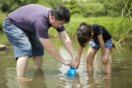 Young Asian father and daughter bonding catching fishes in riverの写真素材