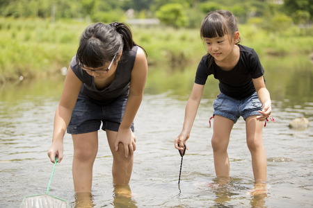 Young Asian girls catching fishes in riverの写真素材