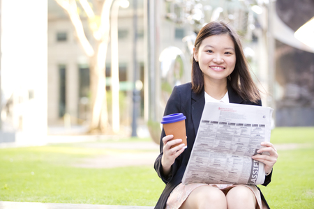 Young Asian female executive drinking coffee and reading newspaperの写真素材