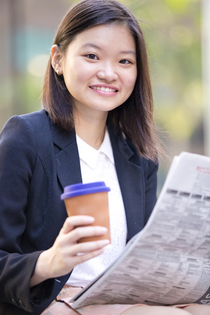 Young Asian female executive drinking coffee and reading newspaperの写真素材