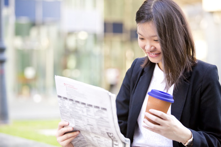 Young Asian female executive drinking coffee and reading newspaperの写真素材
