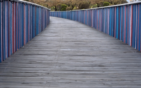 A wide wooden walkway with brightly-colored side rails curves away in the distanceの写真素材