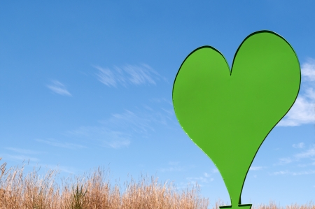A large green heart made of steel sits in a field of grass on a sunny dayの写真素材