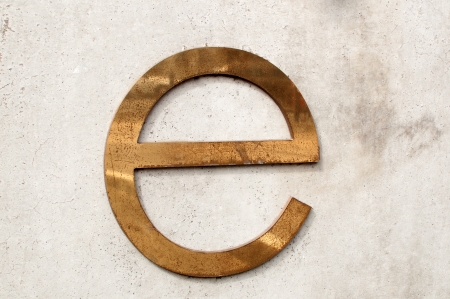 A dirty and tarnished metallic letter e on a gray concrete wallの写真素材