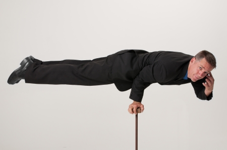 A handsome businessman talks calmly on his telephone while balancing with one arm on a small postの写真素材