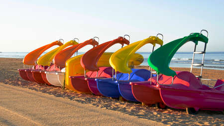 Group of colored pedal boats with slide parked on the beach waiting to be rentedの写真素材