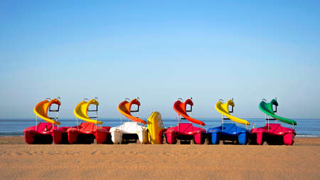 Group of colored pedal boats with slide parked on the beach waiting to be rentedの写真素材