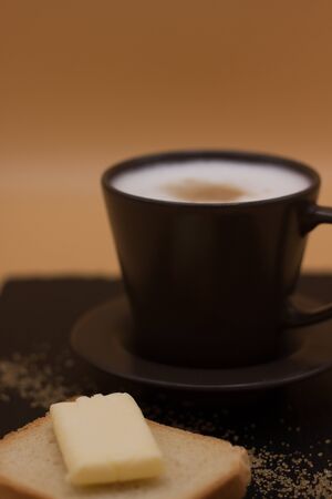 White coffee and toast with butter and sugar. Breakfast in black tray on orange background....