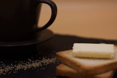 White coffee and toast with butter and sugar. Breakfast in black tray on orange background....