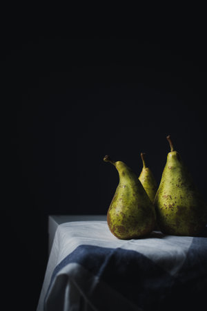 Three pears on a white tablecloth. Dark background. Toned.の写真素材