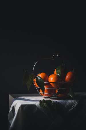 Ripe tangerines with leaves in glass vase on tableの写真素材