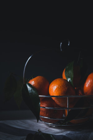 Ripe tangerines with leaves in a metal basket on a dark backgroundの写真素材