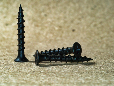 Macro view of black screws background - A detailed, close-up view of a pile of black screws,...