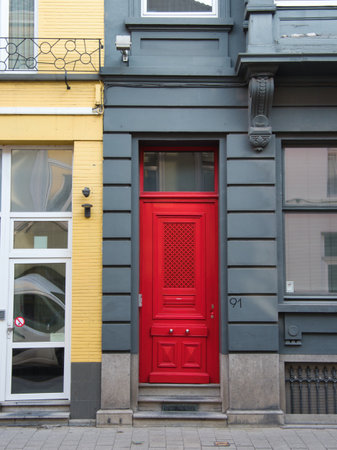 Vibrant Red Door on a Gray Facade - A bright, bold red door with a geometric pattern and shiny door handles stands out against a contrasting gray facade in Ghent, Belgium.の写真素材