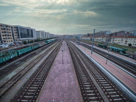 Busy Railroad Tracks in Urban Center - A high-angle shot of multiple railway tracks and platforms converging into the distance, with city buildings and cargo wagons under a dramatic, cloudy sky.の写真素材