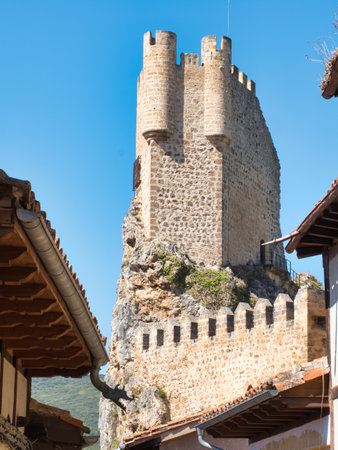 Medieval Fortress of FrÃ­as with Gargoyle - The imposing medieval tower of the castle in FrÃ­as is framed by a traditional building with a unique gargoyle on the roof.の写真素材