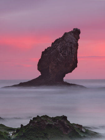 Dramatic Pink Sunset Sky over Buelna Stack - Spectacular long exposure of the iconic sea stack at Buelna Beach, Asturias, silhouetted against a vibrant magenta and pink twilight sky.の写真素材